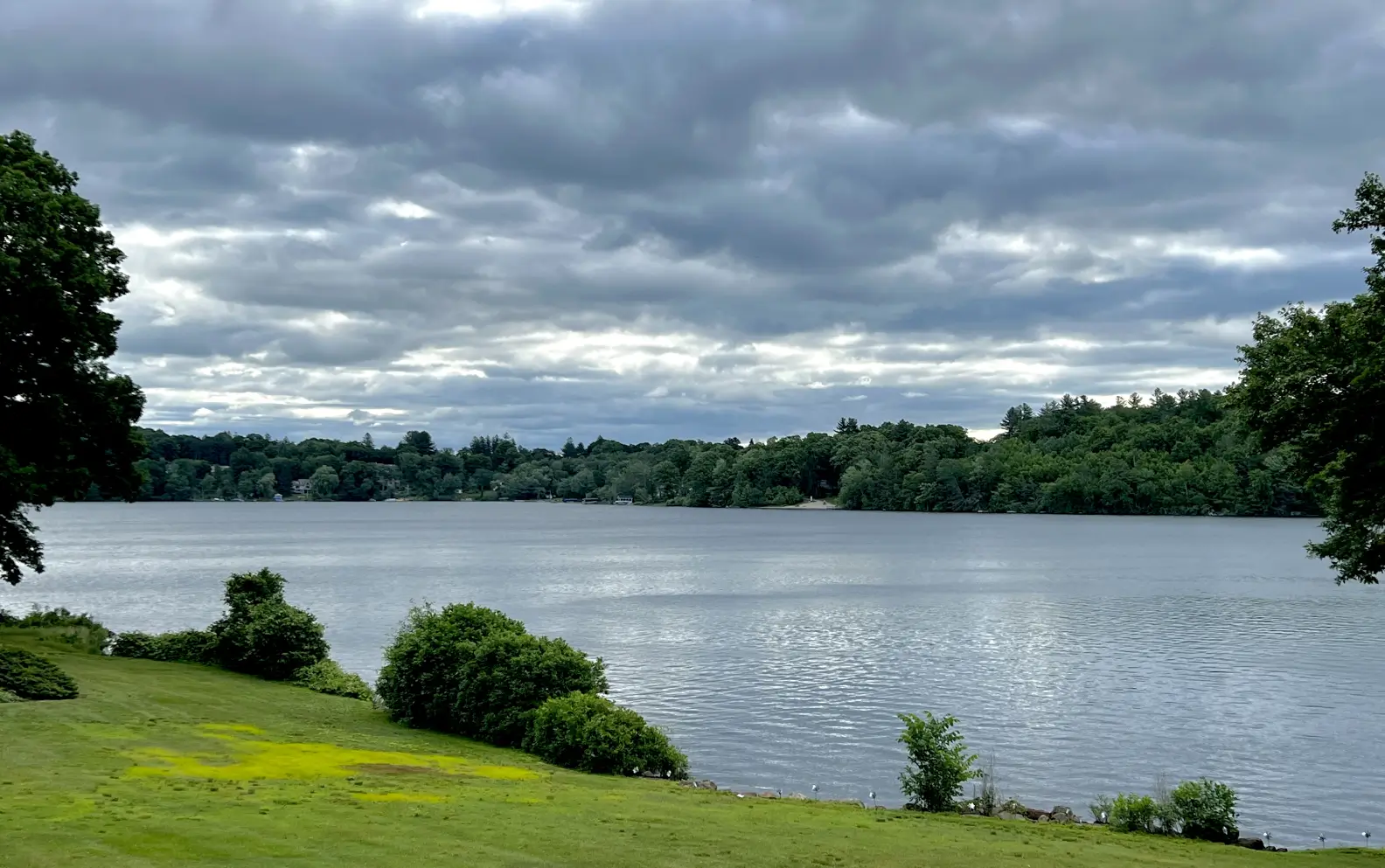 A calm lake under a cloudy sky with surrounding greenery.